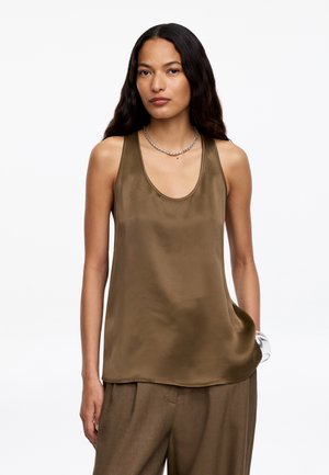 Mujer con cabello largo y oscuro, vistiendo un top sin mangas de satén color oliva y pantalones anchos a juego, complementados con un collar y una pulsera de cadena.
