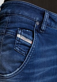 Tmavě modré džíny vyrobené z denimu s malou kapsou se znakem Diesel, kovovým zapínáním a viditelnými stehy.