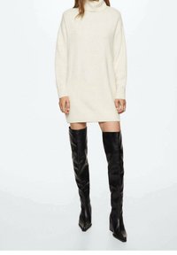 Crème, oversized coltrui jurk met geribbelde manchetten; gecombineerd met hoge, zwarte, glanzende, boven de knie hakken.