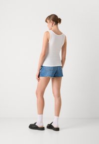 Hvit ribbet tank topp paret med blå denim shorts. Sorte slip-on sko, hvite sokker, hår stylet i en lav knute. Enkelt design, tettsittende.