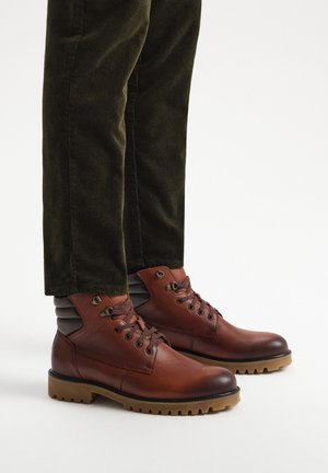 Brązowe skórzane botki za kostkę z teksturowanym wykończeniem, z czarnymi akcentami, sznurowanym przodem i solidną gumową podeszwą.