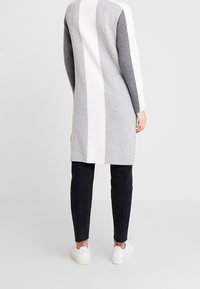 Vestido de suéter largo de punto en gris con franjas verticales en blanco y gris oscuro, que presenta un corte recto, textura acanalada y aberturas laterales.