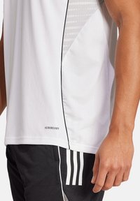T-shirt de sport blanc avec un motif en mesh gris, des accents noir et une étiquette "AEROREADY". Le t-shirt présente une coupe moderne et est conçu pour la performance.