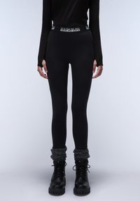 Leggings noirs avec une taille de marque, associés à des jambières en tricot grises épaisses et des bottes noires à lacets avec une semelle épaisse.