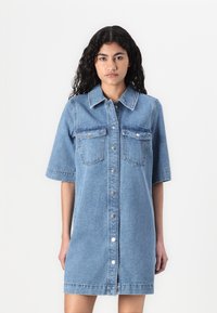 Φόρεμα πουκαμίσα από τζην σε ανοιχτό μπλε, διαθέτει κοντά μανίκια, γιακά, κλείσιμο με κουμπιά μπροστά και δύο τσέπες στη στήθη με ασημένια κουμπιά.