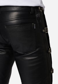 Zwarte leren broek met een getailleerd ontwerp, zijklittensluiting en een achterzak met gestikte details. Glad oppervlak overal.