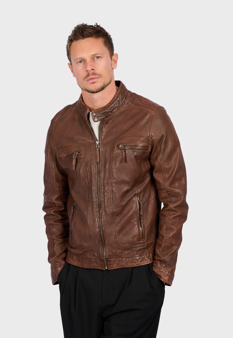 Giacca in pelle marrone con un design aderente, chiusura con zip e due tasche sul petto. Caratterizzata da un colletto alla stirpe e una texture liscia.
