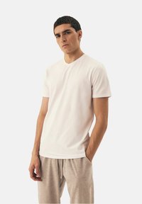 Biała koszulka krótki rękaw z dekoltem w serek, gładka tekstura, dopasowany krój, zestawiona z jasnoszarymi spodniami w luźnym fasonie.