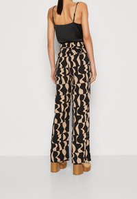 Vida byxor i svart och beige mönster, med flödande tyg, hög midja och en slät yta. Matchas med en figurnära svart topp.