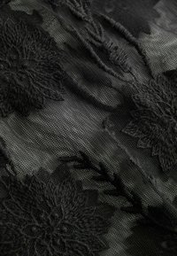 Tessuto nero trasparente con grandi motivi floreali ricamati e dettagli strutturati che creano un design stratificato e delicato.