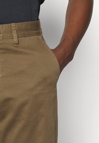 Khakifärgade byxor med rak framdel och sidofickor, tillverkade av ett mjukt tyg. Har subtila sömmar och en avslappnad passform.