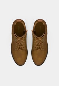 Botines de cuero marrón con punteras redondeadas, cordones planos y un tacón pequeño. Textura suave con un brillo sutil y el logo de la marca en el interior.