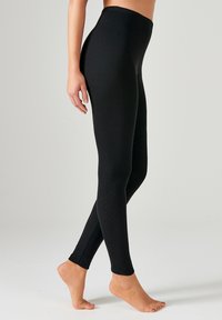 Leggings negros hechos de material elástico, con una textura suave, cintura alta y un diseño ajustado, que llega hasta el tobillo.