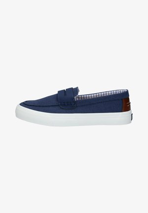 Scarpa slip-on in tela blu navy con suola in gomma bianca. Presenta cuciture decorative e un accento in pelle marrone sul tallone. Interno a righe.
