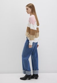 Gestreifter Strickpullover in Rosa, Weiß und Braun, kombiniert mit lockeren blauen Jeans. Schwarze Stiefeletten mit Absatz. Seitenansicht mit glattem Haar.