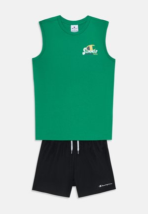Top din bumbac verde fără mâneci cu grafică "SUMMER", asociat cu pantaloni scurți negri cu șnur alb și logo pe tiv.