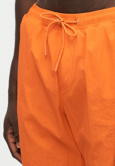 Gros plan d'une personne portant un short à cordon orange vif avec une taille élastique et un nœud noué à l'avant.