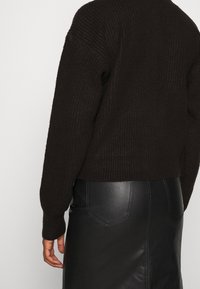 Hnědý žebrovaný pletený svetr s kleslými rameny, spárovaný s černou koženou sukní s viditelným šitím a náprsními kapsami.