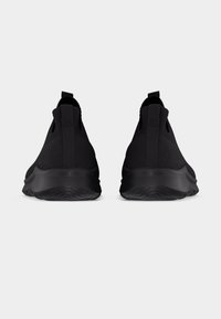 Ζευγάρι μαύρα αθλητικά παπούτσια slip-on με πλεκτό ύφασμα και ανάγλυφες λαστιχένιες σόλες, από την πίσω πλευρά, σε απλό φόντο.