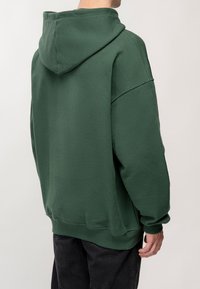 Zelená bavlněná mikina s kapucí, oversized střih a žebrované manžety. Hladká textura, minimální šití a jednobarevný design.