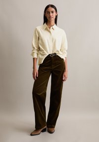 Yellow checkered button-up shirt, black belt, and wide olive green corduroy pants. Brown heeled shoes complete the outfit.