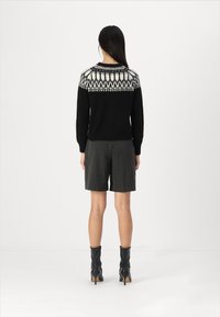 Svart tröja med vit mönstrad ok; ribbade ärmar; kombinerad med grå shorts; avslutad med svarta klackboots; slät textur.