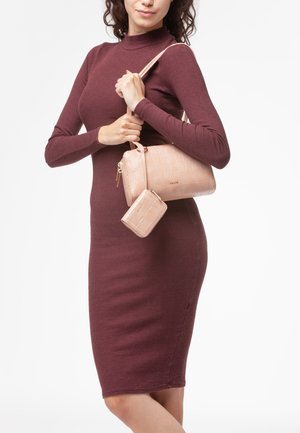 Borsa a mano testurizzata di un rosa chiaro con un motivo a griglia e hardware dorato, accompagnata da un piccolo portafoglio abbinato. Il modello indossa un vestito a coste bordeaux.