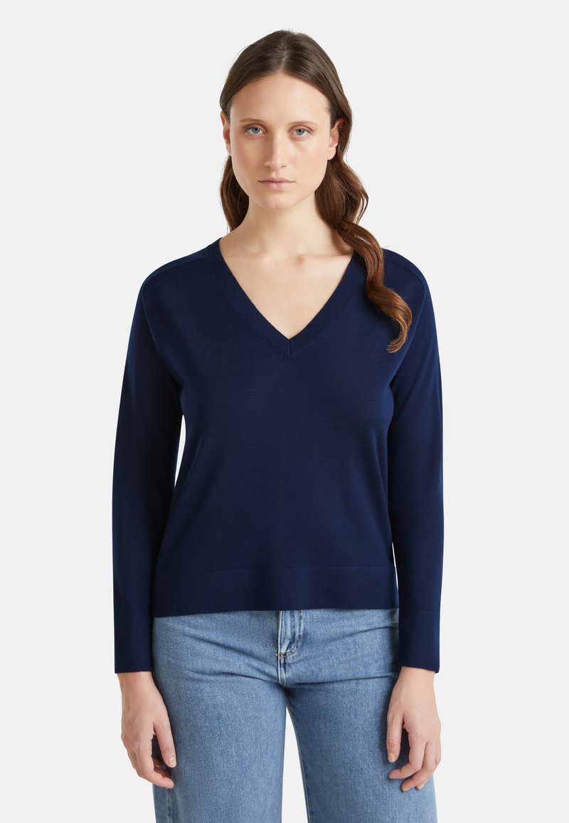 Pull à col en V navy à manches longues, fabriqué dans un tissu doux, avec une coupe décontractée et une texture lisse. Associé à un jean en denim.