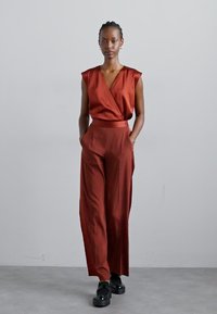 Rød sateng jumpsuit med omslagdesign, kort ermer, brede ben og belted midje. Kombinert med svarte platåsko.
