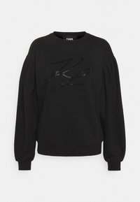 Sweat-shirt noir avec manches longues ballon et col rond. Présente un logo texturé et scintillant sur le devant. Tissu doux et uni.
