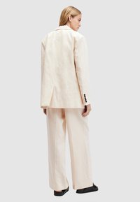 Completo color crema a righe con blazer strutturato e pantaloni a gamba larga. Il blazer presenta un collo a bavero e bottoni neri.