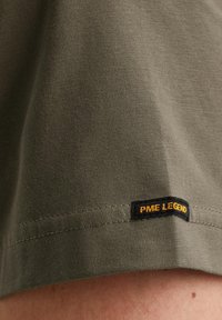 Maslinasto zeleni pamučni majica s glatkom teksturom, s crnom oznakom na rubu na kojoj je žutim koncem ušiveno "PME LEGEND".