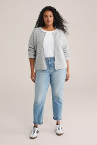Lysegrå strikket cardigan med rund hals, knaplukning og dropped shoulders, båret over en hvid skjorte og lyseblå jeans med opsmøg.