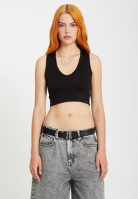 Débardeur noir côtelé avec un décolleté en V, présentant une silhouette ajustée et une texture lisse. Assorti à un pantalon en denim taille haute gris et une ceinture noire.