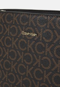 Černá texturovaná peněženka s embosovaným vzorem loga v hnědé barvě. Zlaté akcenty loga "Calvin Klein" doplňují design.
