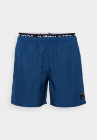 Blue swim shorts with an elastic waistband featuring a black brand label. Material is smooth with a lightweight texture. Simple design.