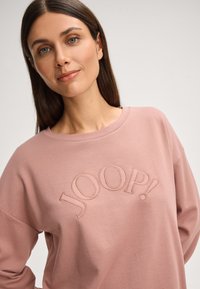 Lichtroze sweatshirt met een gebogen geborduurd logo "JOOP!" in een bijpassende tint. Zachte textuur met een comfortabele pasvorm en een brede halslijn.