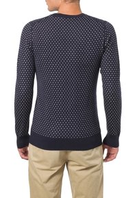 Marinblå stickad tröja med små vita prickar, ribbade muddar och nederkant, rund hals, figurnära design. Strukturerad tyg förbättrar detaljer.