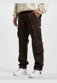Pantalones cargo marrones con múltiples bolsillos laterales, de corte relajado, fabricados con tejido duradero. Combinados con zapatillas blancas.