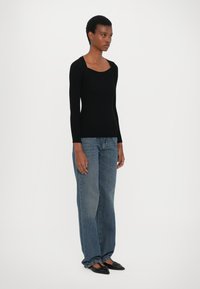 Svart ribbet langermet topp med vid halsutskjæring, kombinert med løse, lyseblå denimjeans og svarte spisse flats.