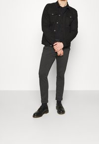 Svart denimjacka med knappstängning, grå tapered byxor och svarta snörskor. Slät textur, figursydd design och uppvikta ärm på byxorna.
