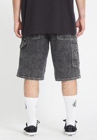 Shorts cargo en denim noir avec une texture délavée, des poches latérales et des coutures contrastées. Associés à des chaussettes blanches côtelées et des baskets noires.