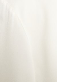 Gros plan sur un tissu lisse de couleur crème avec une couture subtile créant un pli doux.