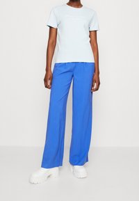 Camiseta de manga corta azul claro con logo, combinada con pantalones anchos de un azul brillante y zapatillas de plataforma gruesa blancas. Diseño simple y moderno.