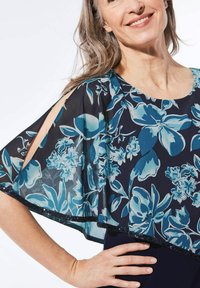 Blumige Überlagerung in Blautönen auf einem navyfarbenen Grund, mit transparenter Stoffqualität, gewelltem Saum und Paillettenakzenten entlang des Randes.