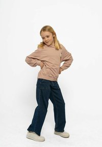Sudadera con capucha de color rosa claro con puños y cinturilla elásticos, que presenta un diseño de cono de helado. Combinada con pantalones vaqueros anchos azules y zapatillas blancas.
