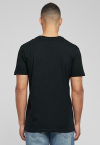Camiseta negra de manga corta con cuello redondo, fabricada en algodón, que presenta una textura suave y un diseño minimalista. Se muestra la vista desde atrás.