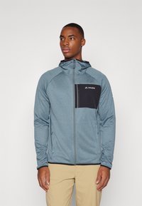 Giacca in fleece di colore blu mélange con una tasca sul petto con zip nera, cappuccio aderente e orlo nero a contrasto. Presenta una chiusura con zip e un tessuto testurizzato.