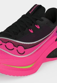 Ροζ και μαύρο παπούτσι για τρέξιμο με μαύρα κορδόνια, άνω μέρος από διαπνέον διχτυωτό υλικό και καμπύλη σόλα με πράσινες και μαύρες λεπτομέρειες.