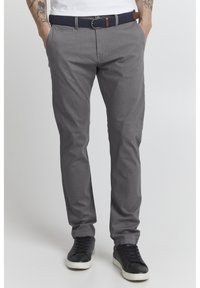 Chinos grises hechos de tela ligera con un diseño slim-fit, que cuentan con bolsillos laterales y un cinturón trenzado en navy. Combinados con zapatillas negras.